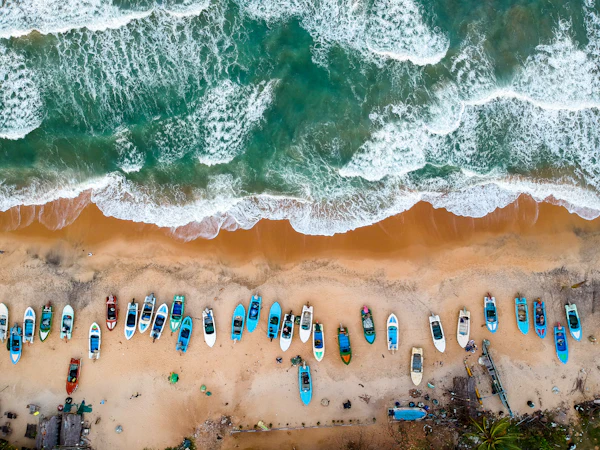 Aerial view of colourful fishing boats pulled up on a sandy beach as waves roll in