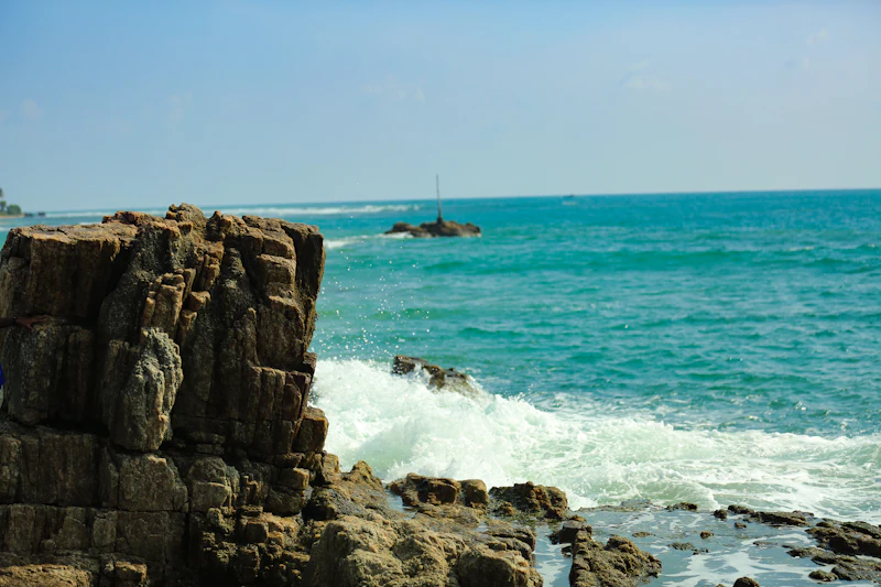 Waves breaking against dark rocks beside a clear turquoise sea