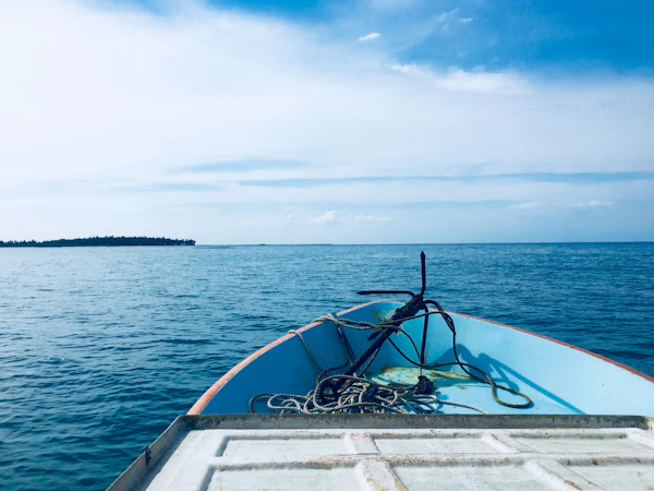 The bow of a small boat heading out across calm, clear blue water