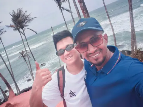 A guest and their driver-guide taking a selfie above the sea, with tall palms behind