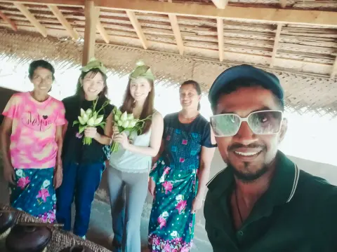 Guests holding white lotus flowers under a thatched roof, with their driver-guide in front