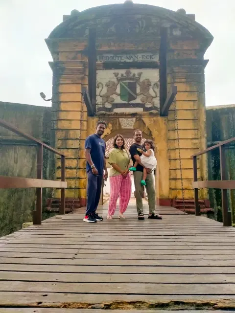 A family on a wooden bridge in front of an old stone gateway topped with a coat of arms
