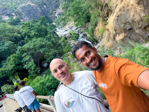 A guest and their driver-guide taking a selfie above a waterfall in a forested gorge