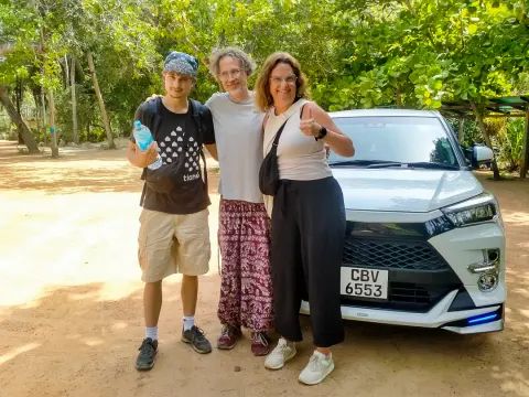 Three guests standing beside a white car on a sandy forest track