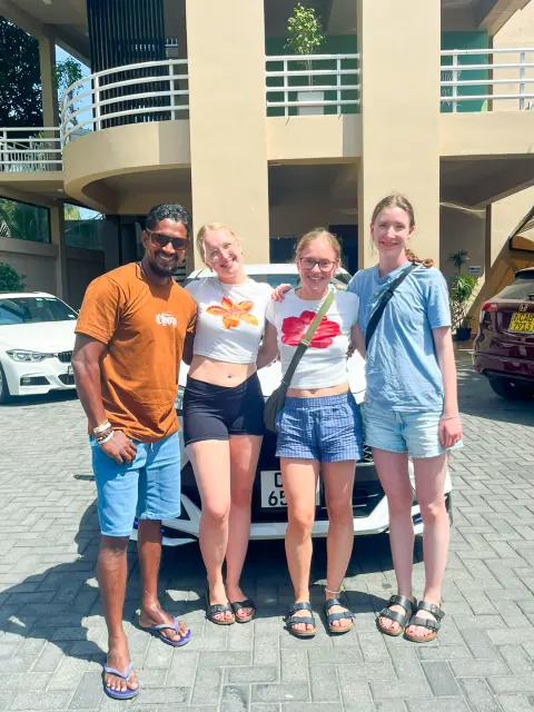 Three guests and their driver-guide standing by a car outside a hotel