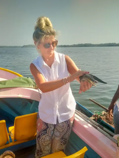 A guest standing in a small boat on wide, calm water, holding up a small catch
