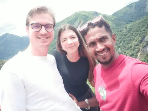 Two guests and their driver-guide taking a selfie in front of green mountains