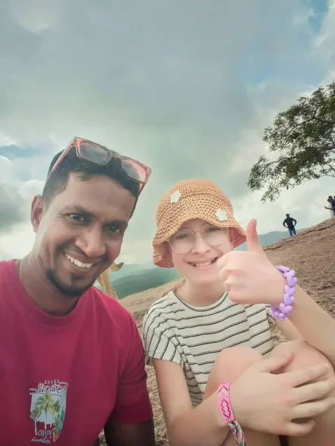 A young guest giving a thumbs-up beside their driver-guide on a rocky hilltop