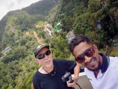 A guest with a camera and their driver-guide taking a selfie high above a green valley with a waterfall