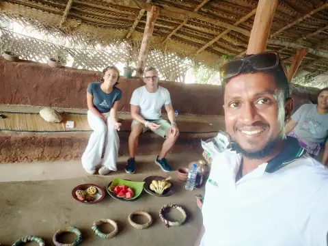 Two guests seated in a thatched hut with dishes laid out in clay bowls on the floor, and their driver-guide in front