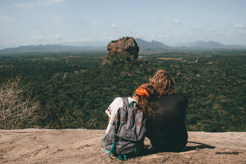 A couple sitting on a rock, looking out across the forest to Sigiriya rock fortress