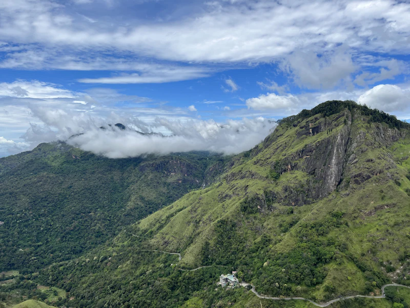 Steep green mountain slopes under a blue sky with drifting cloud