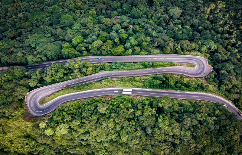 Aerial view of a winding road with hairpin bends through dense green forest