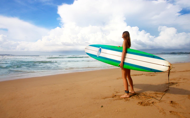A surfer holding a longboard on the beach, with waves rolling in behind