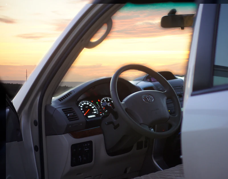 View through an open car door to the steering wheel, with a sunset sky beyond
